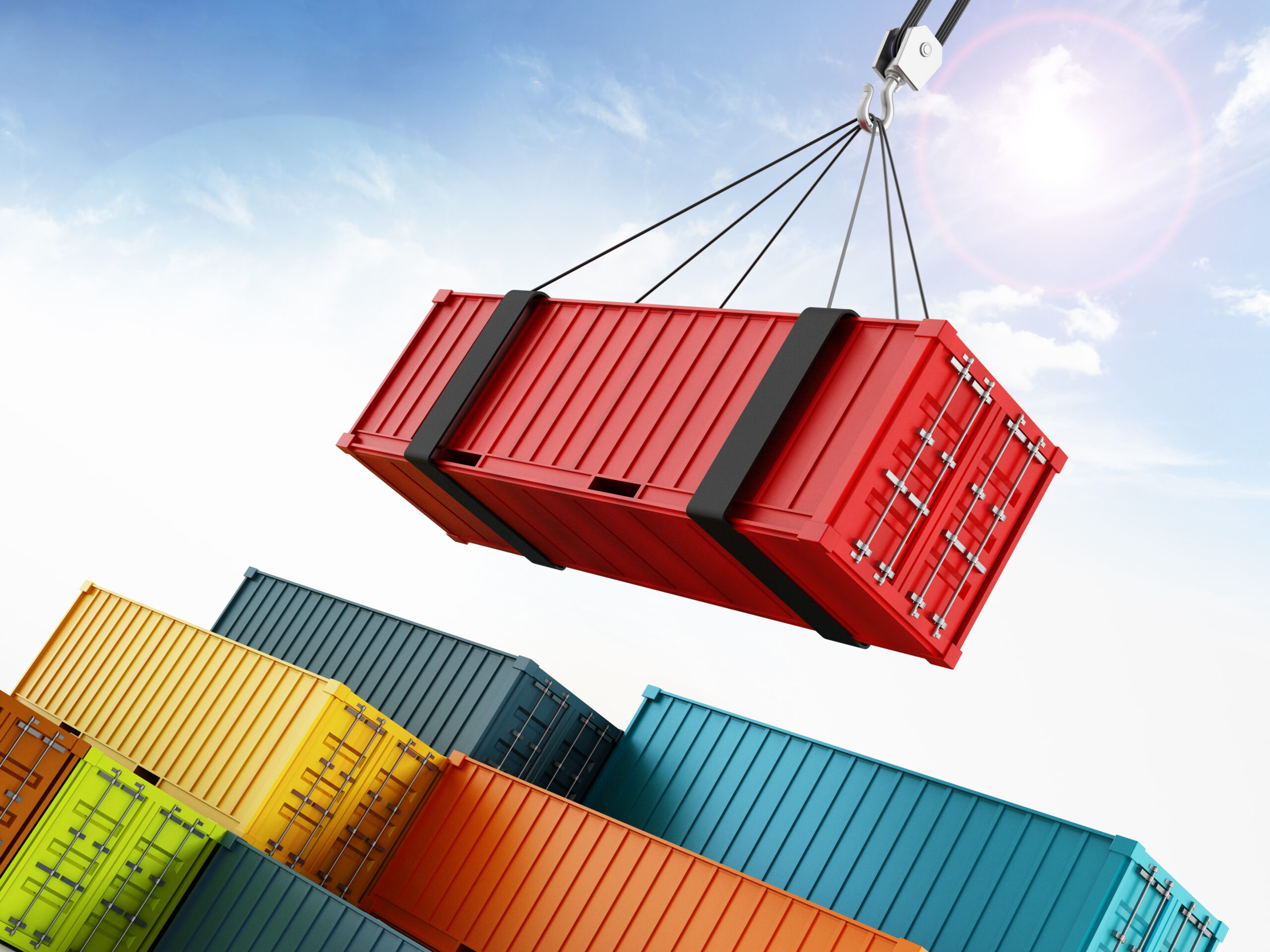 A crane hoists a red shipping container above stacks of colorful cargo containers against a bright blue sky.