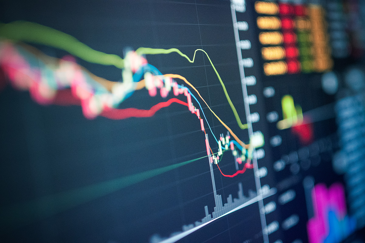 Close-up of a financial trading screen displaying colorful candlestick charts and trend lines on a dark background.