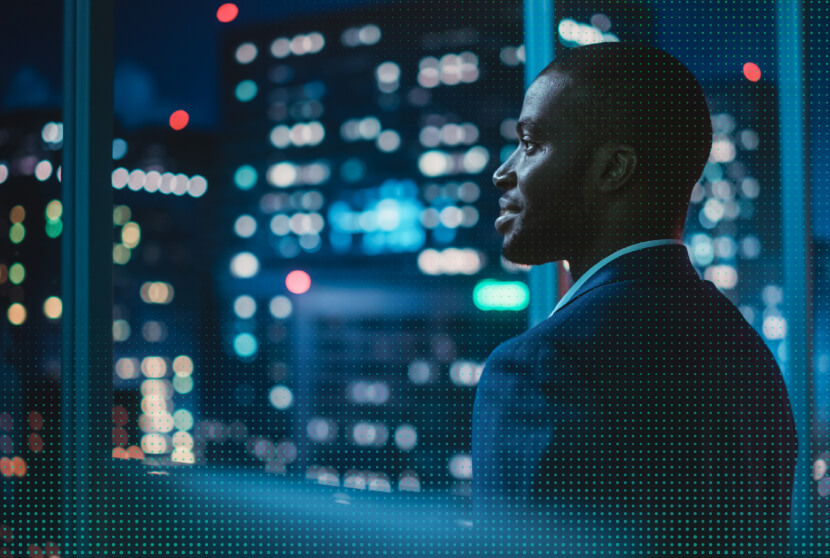 Businessman in a suit gazing out a window at a blurred cityscape illuminated by night lights.