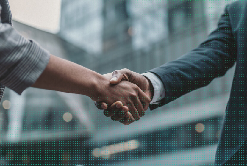Two professionals in business attire shake hands, symbolizing partnership or agreement against a blurred urban background.