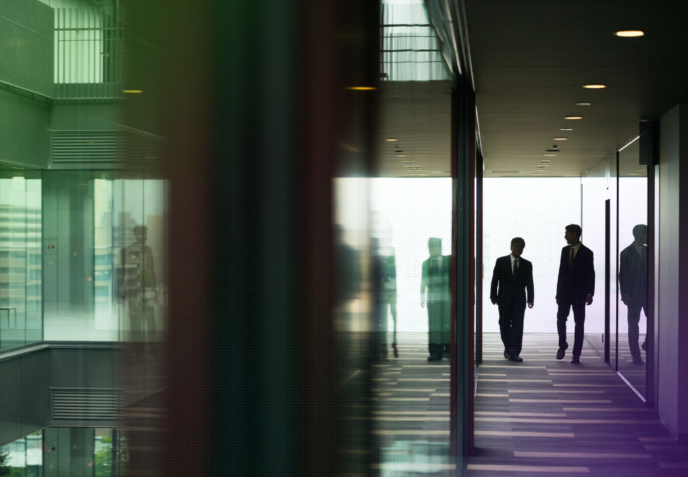 Silhouetted businessmen in suits walking through a modern glass corridor with colorful reflections and ambient lighting.