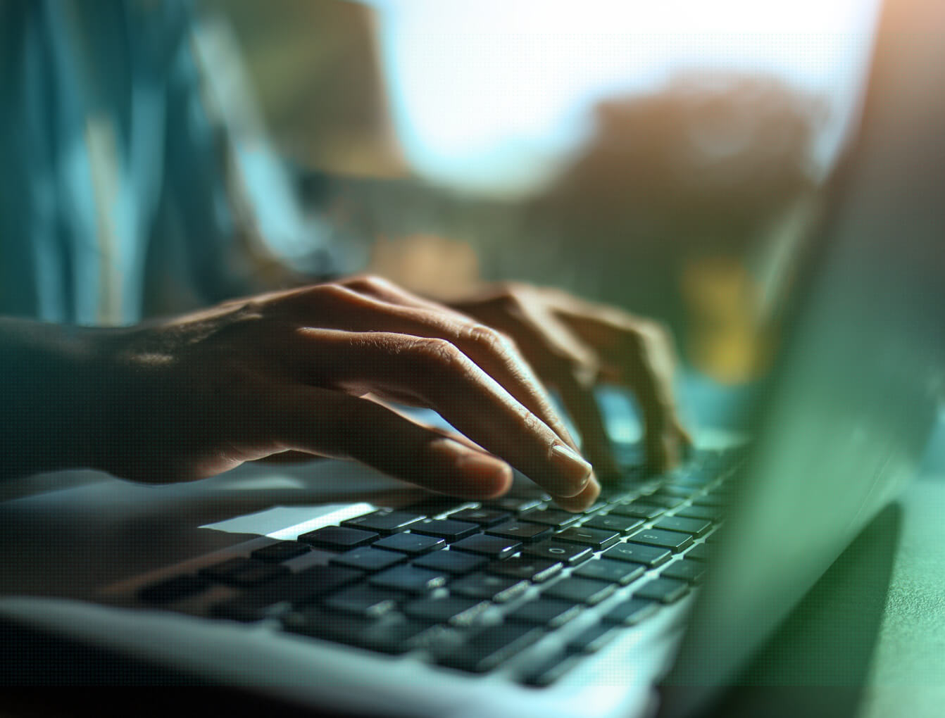 Close-up of hands typing on a laptop keyboard with a softly blurred outdoor background.