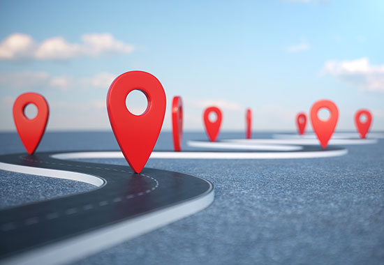 Red location pin markers line a winding road under a blue sky, symbolizing a strategic journey or roadmap.