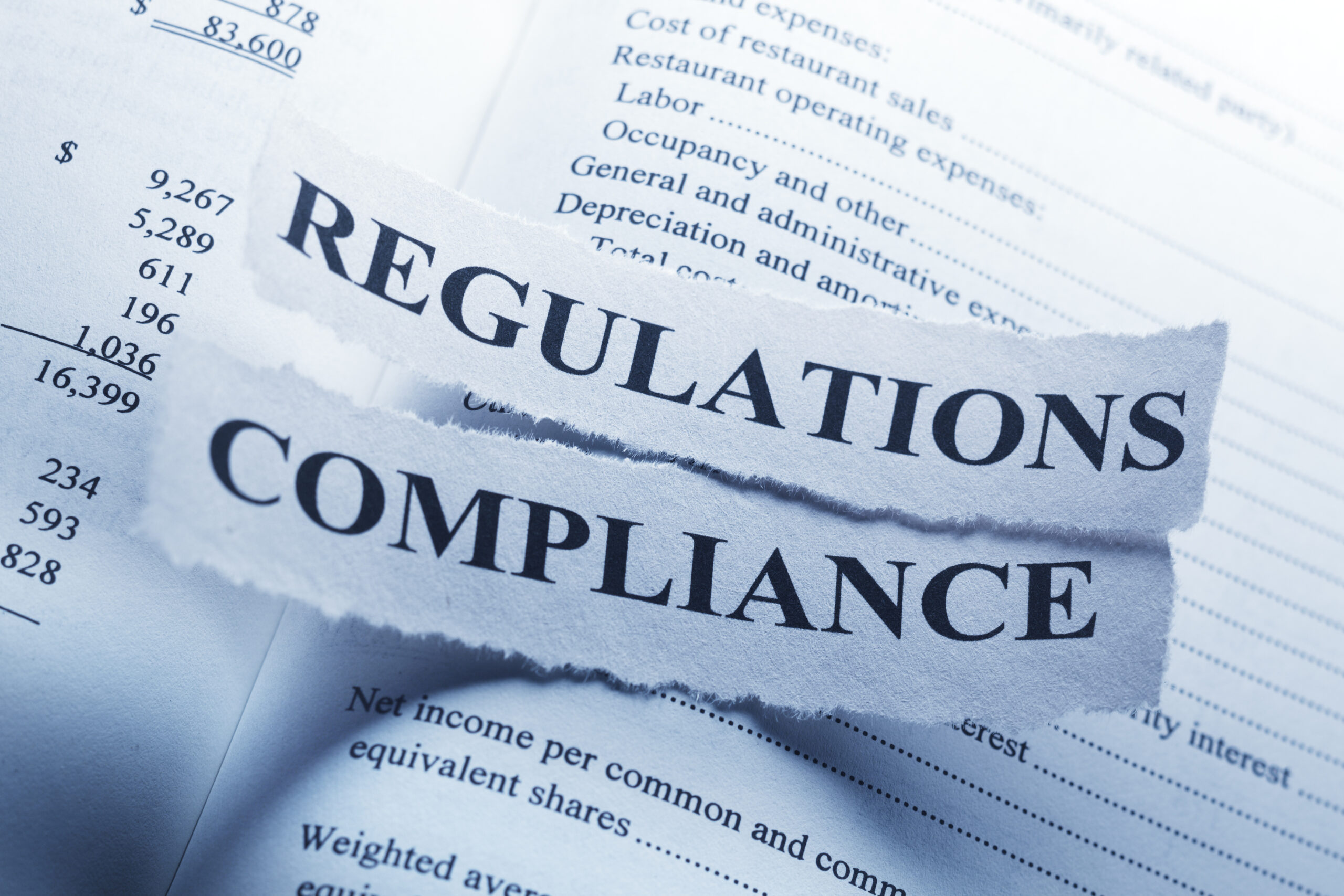 Torn paper clippings with the words "Regulations" and "Compliance" laid over a financial statement listing expenses and