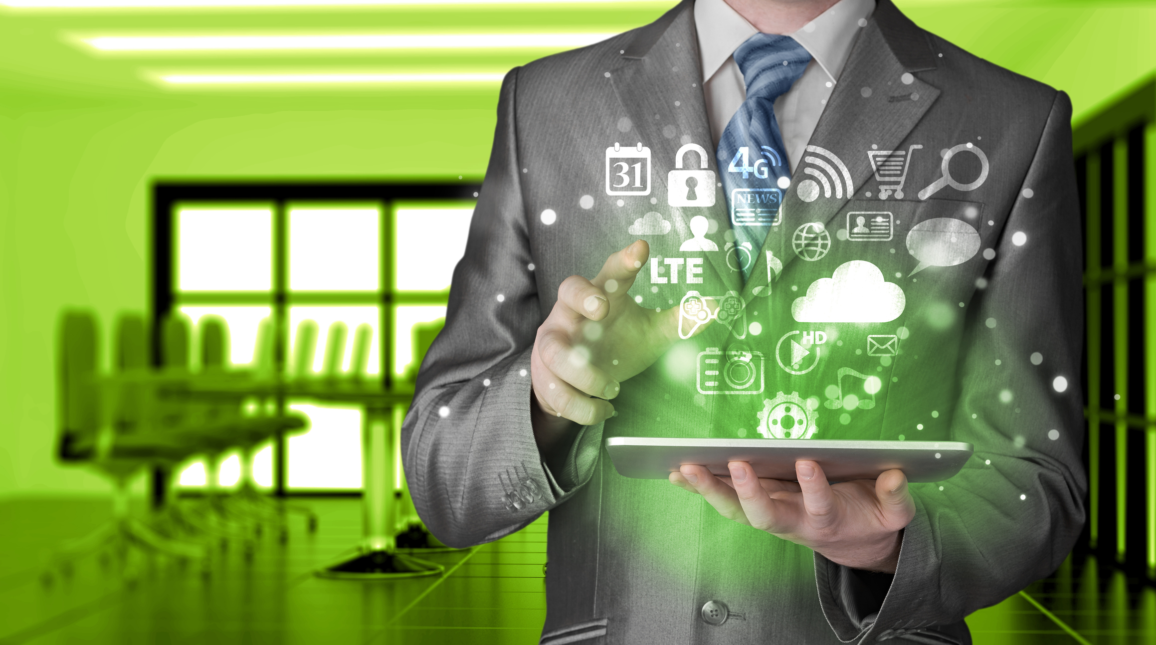 Businessman in a gray suit holding a tablet with digital app icons floating above it in a green-tinted office.