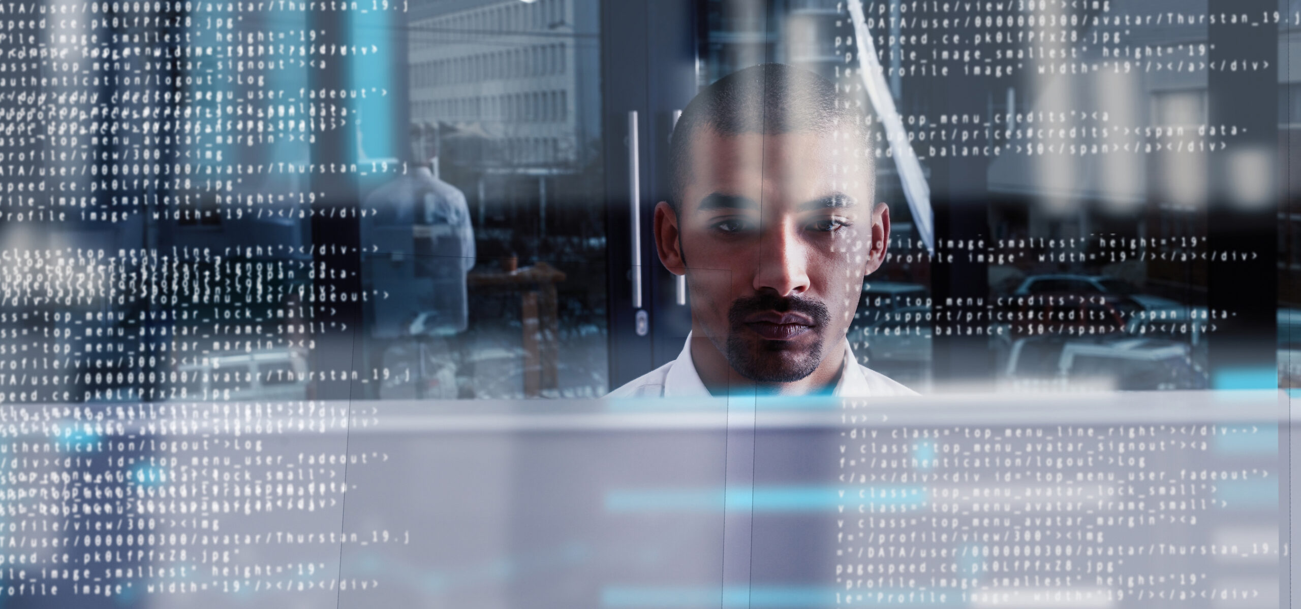 Focused man with mustache working behind a screen of overlaid code, reflecting deep concentration in a tech environment.